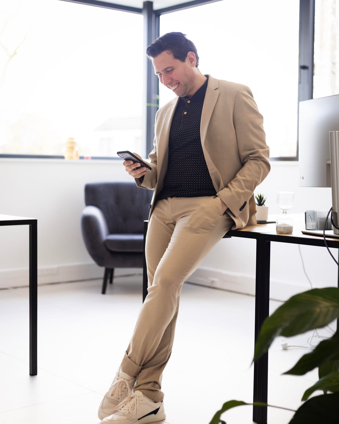 Grégory Di Palma, adossé à son bureau, consulte son téléphone en souriant dans un espace de travail lumineux